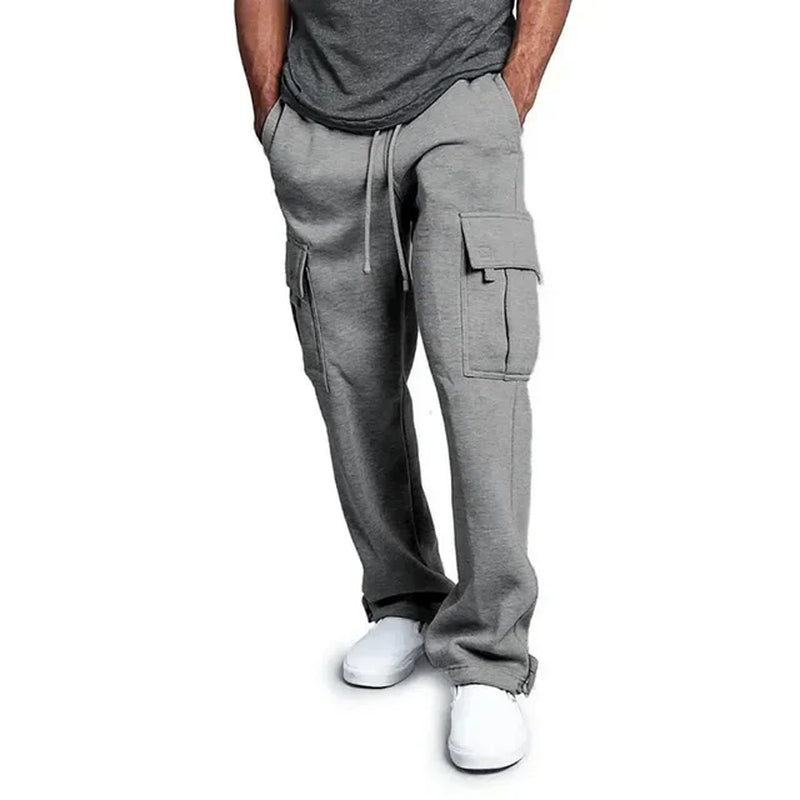 Pantalon cargo gris pour homme avec poches latérales, style décontracté, cordon de serrage, porté avec des baskets blanches. Mode masculine tendance.