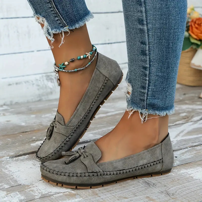 Chaussures mocassins gris pour femme, en daim, portées avec un jean déchiré. Style décontracté, mode automne, accessoires de cheville.