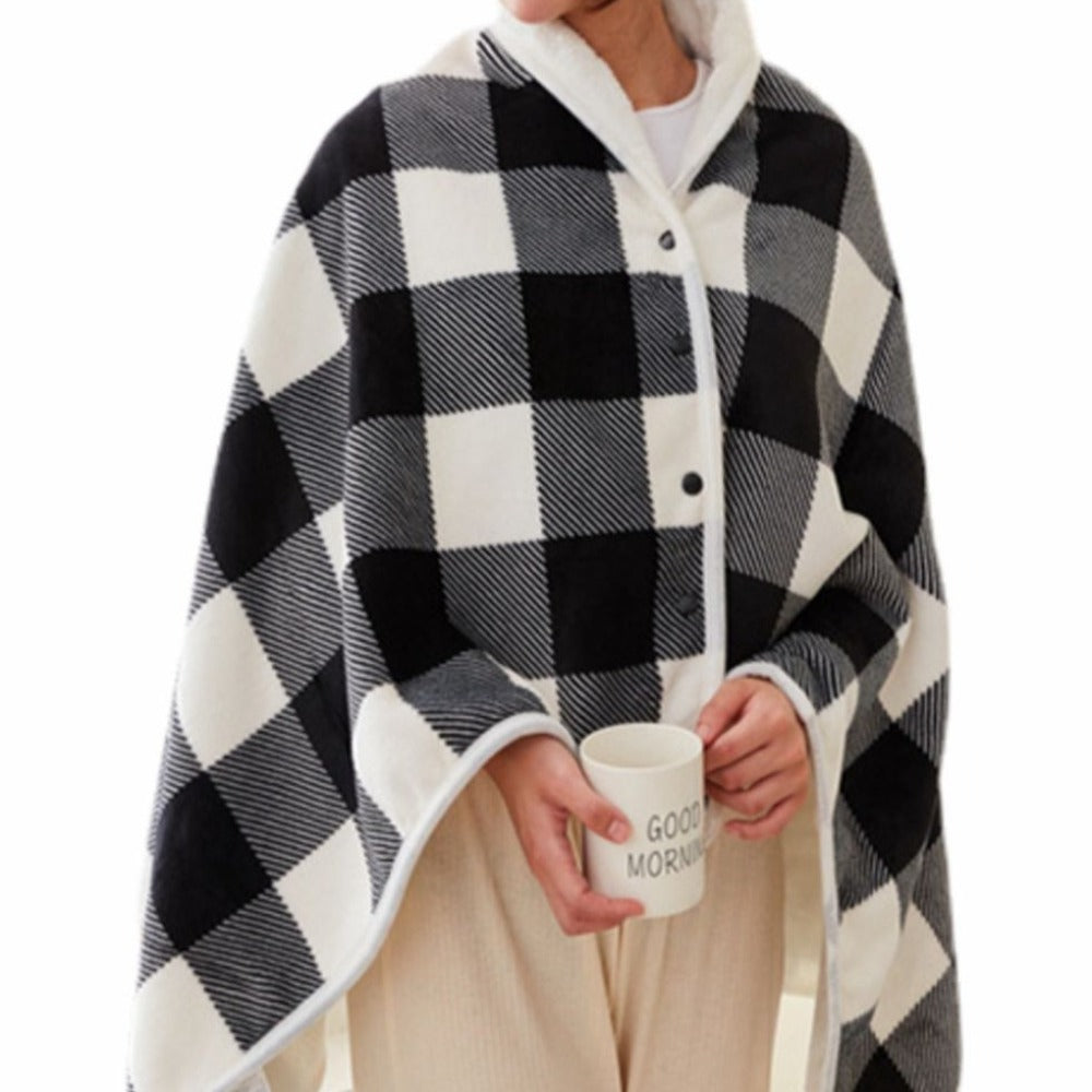 Cape à carreaux noir et blanc, portée par une personne tenant une tasse blanche. Mode hiver, plaid chaud, style cocooning.