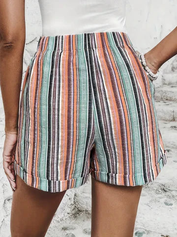 Short en lin rayé multicolore pour femme, motifs vert, orange et noir, style décontracté estival, fond de mur blanc.