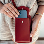 Femme tenant un étui en cuir rouge avec smartphone, robe beige, bague et montre dorée. Accessoire mode pratique et élégant.