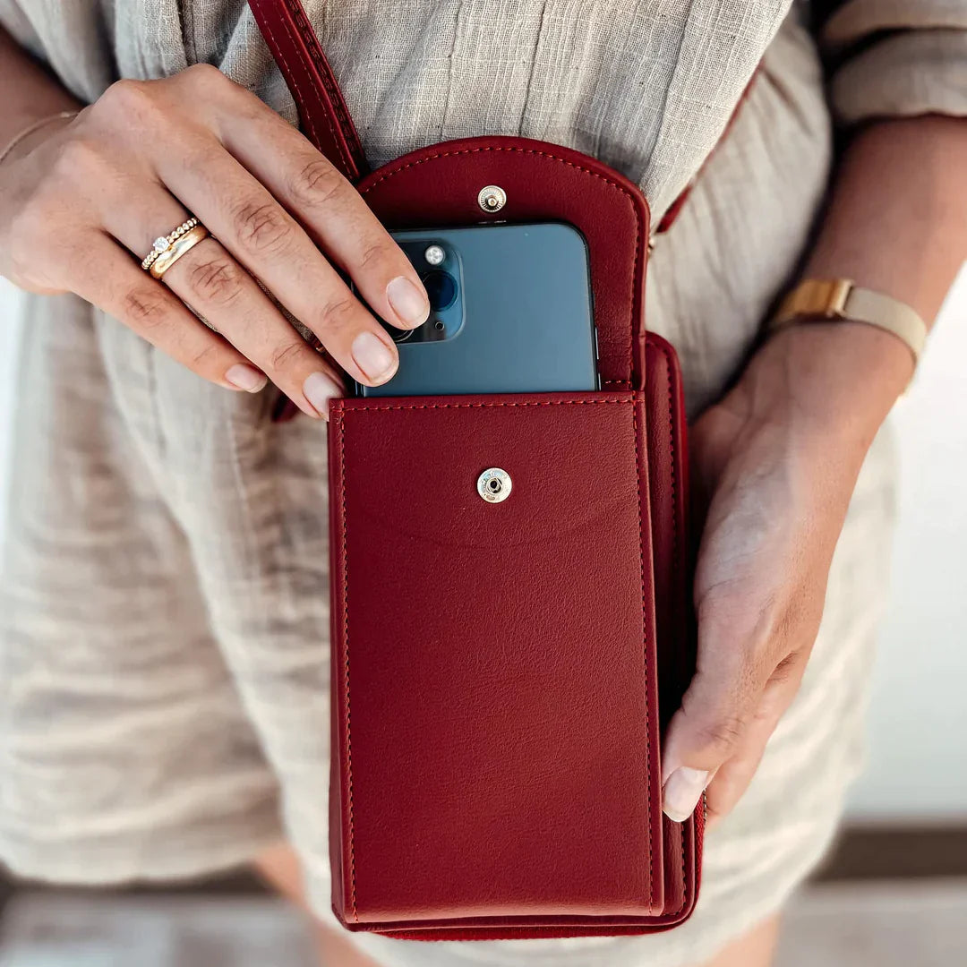 Femme tenant un étui en cuir rouge avec smartphone, robe beige, bague et montre dorée. Accessoire mode pratique et élégant.