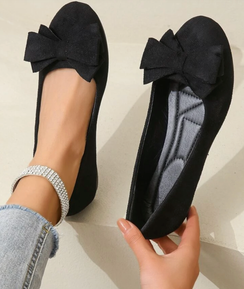 Ballerines noires élégantes avec nœud, portées avec un bracelet en strass et un jean. Chaussures mode femme, style chic et décontracté.