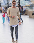 Homme à la mode portant un pull beige, jeans déchirés et baskets dorées, marchant en ville. Style urbain, tendance, look décontracté.