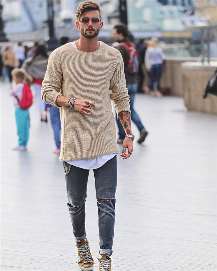 Homme à la mode portant un pull beige, jeans déchirés et baskets dorées, marchant en ville. Style urbain, tendance, look décontracté.