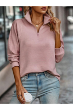 Femme portant un pull rose à col zippé, manches longues, avec un jean bleu clair, tenant un gobelet de café. Mode automne, style décontracté.