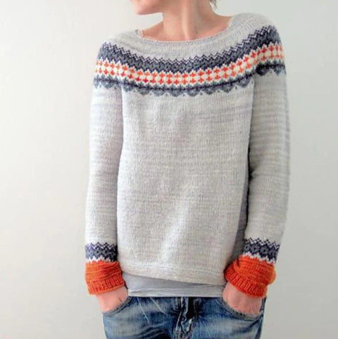 Pull en laine gris avec motifs nordiques colorés, manches longues, poignets orange, porté par une personne en jean. Mode hiver, style scandinave.