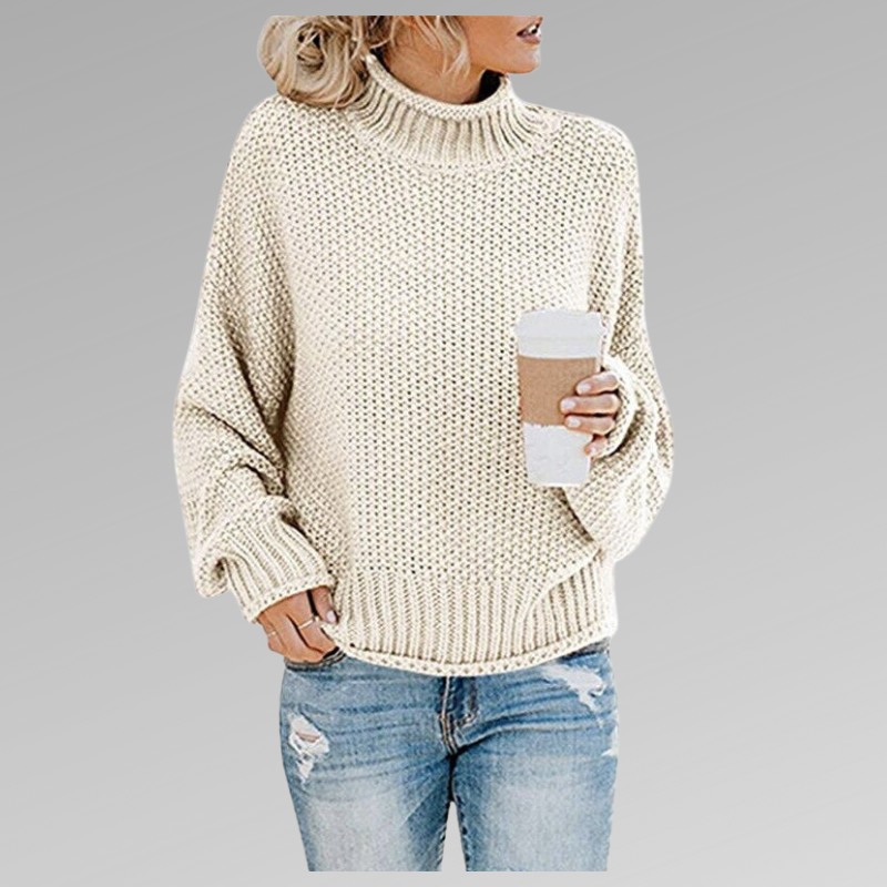 Femme en pull en maille beige, tenant un gobelet de café, portant un jean déchiré. Mode automne-hiver, style décontracté, tendance féminine.