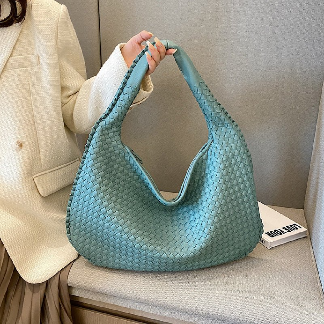 Sac à main tissé bleu-vert élégant, porté par une personne en manteau beige. Accessoire mode tendance, idéal pour un look chic et moderne.