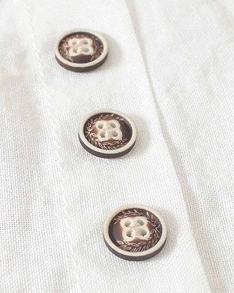 Trois boutons décoratifs en bois sur une chemise blanche en lin, motif floral gravé, style vintage, couture artisanale, mode éco-responsable.