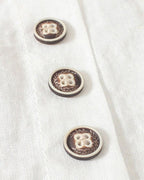 Trois boutons décoratifs en bois sur une chemise blanche en lin, motif floral gravé, style vintage, couture artisanale, mode éco-responsable.