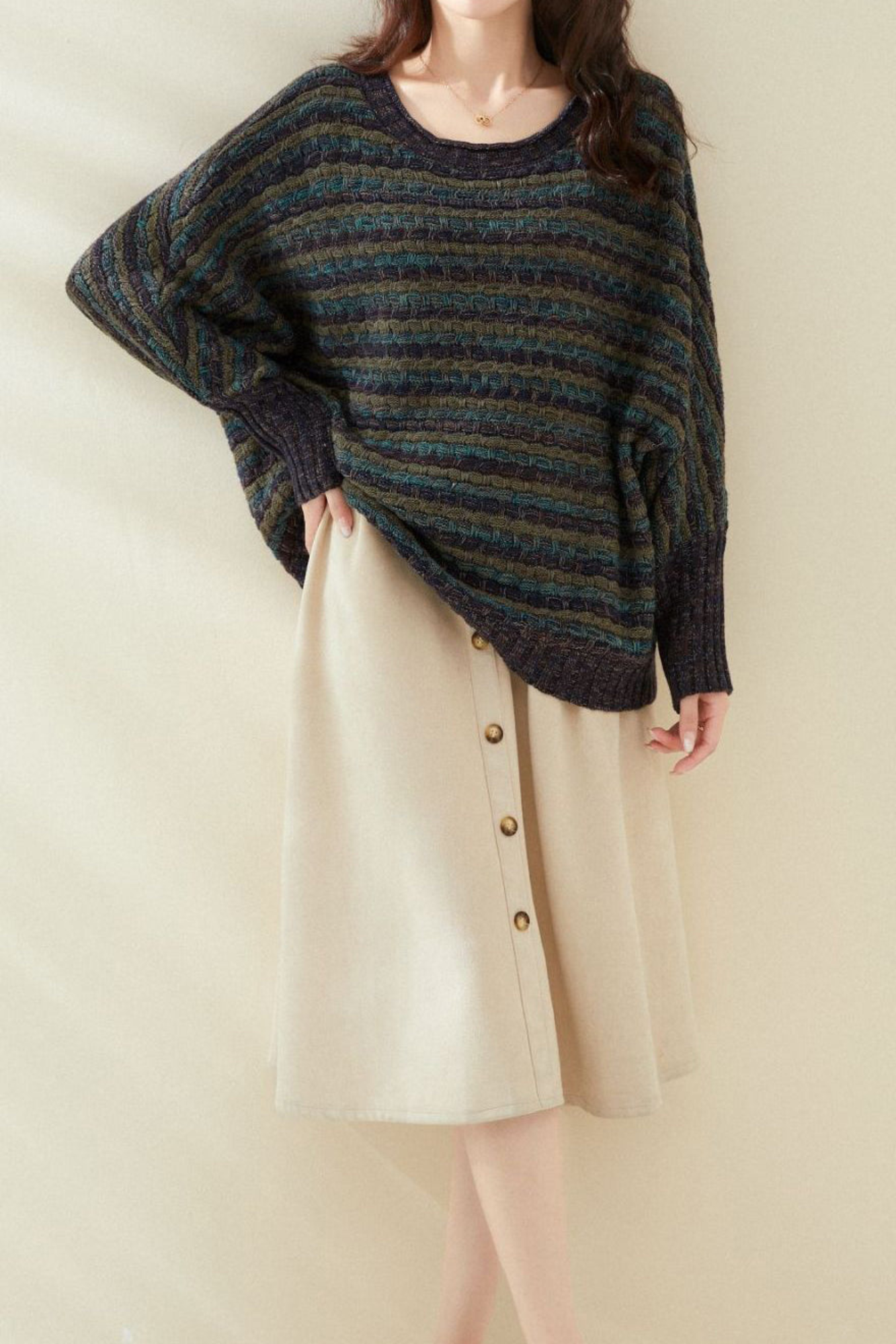 Femme portant un pull rayé ample et une jupe beige à boutons, mode automne-hiver, style décontracté chic, vêtements tendance pour femmes.
