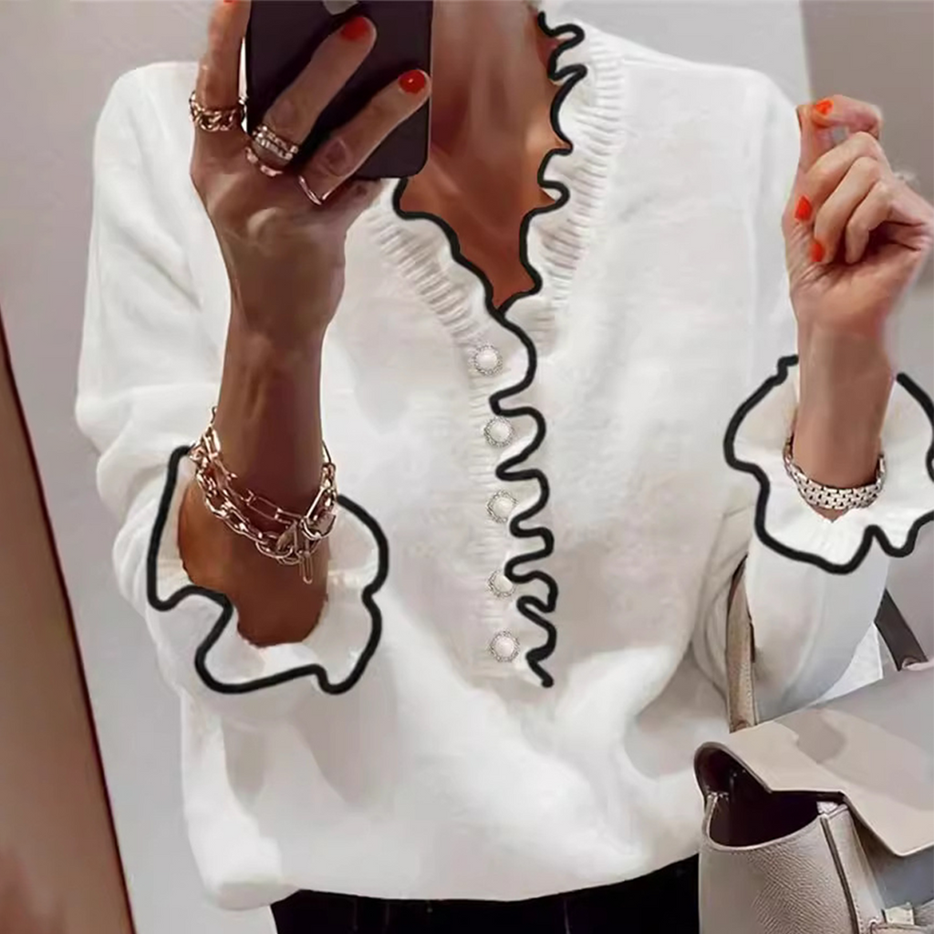 Femme en pull blanc à volants noirs, tenant un smartphone, portant des bracelets dorés, ongles rouges, sac à main beige. Mode élégante et moderne.