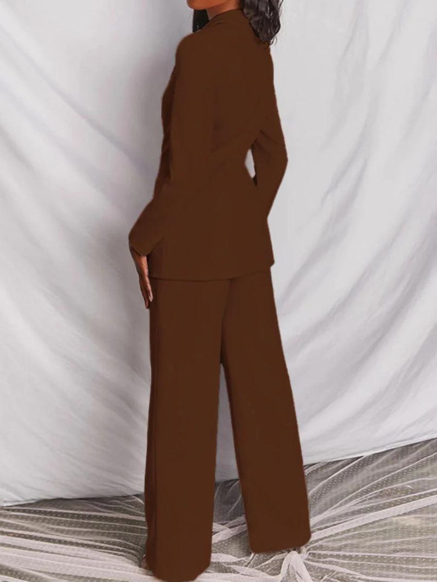 Femme en tailleur marron, posant de dos, sur fond blanc texturé. Mode élégante, costume femme, tendance automne-hiver, style professionnel.