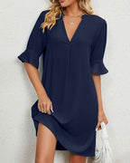 Robe bleu marine élégante avec manches mi-longues et col en V, portée par une femme blonde. Mode féminine chic, tenue décontractée tendance.