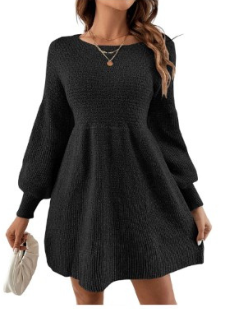 Robe pull noire élégante avec manches longues bouffantes, col rond, portée par une femme tenant un sac à main blanc. Mode automne chic.