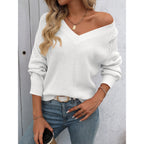 Femme portant un pull blanc en tricot à col en V, manches longues, avec un jean bleu. Accessoires: collier doré, ceinture blanche, boisson à la main.