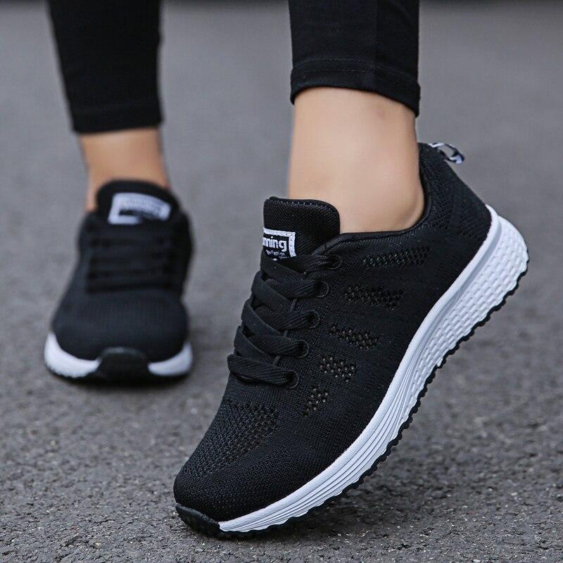 Chaussures de sport noires pour femme, semelle blanche, design respirant, idéales pour la course et le fitness, portées sur une route grise.