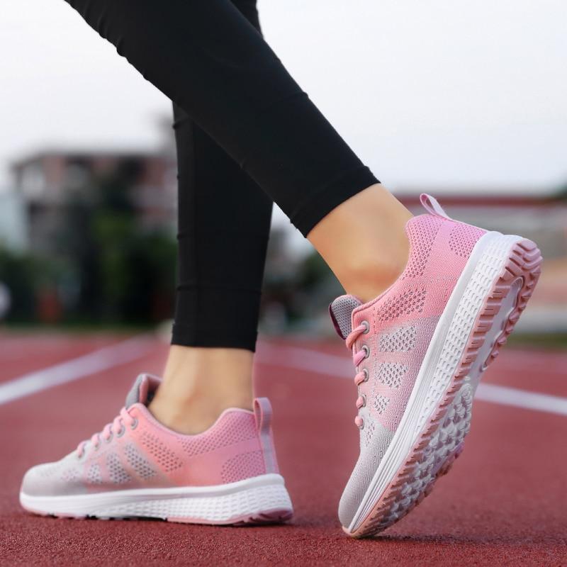 Baskets de course roses et grises sur piste d'athlétisme, femme en leggings noirs, chaussures de sport légères, mode fitness, entraînement extérieur.