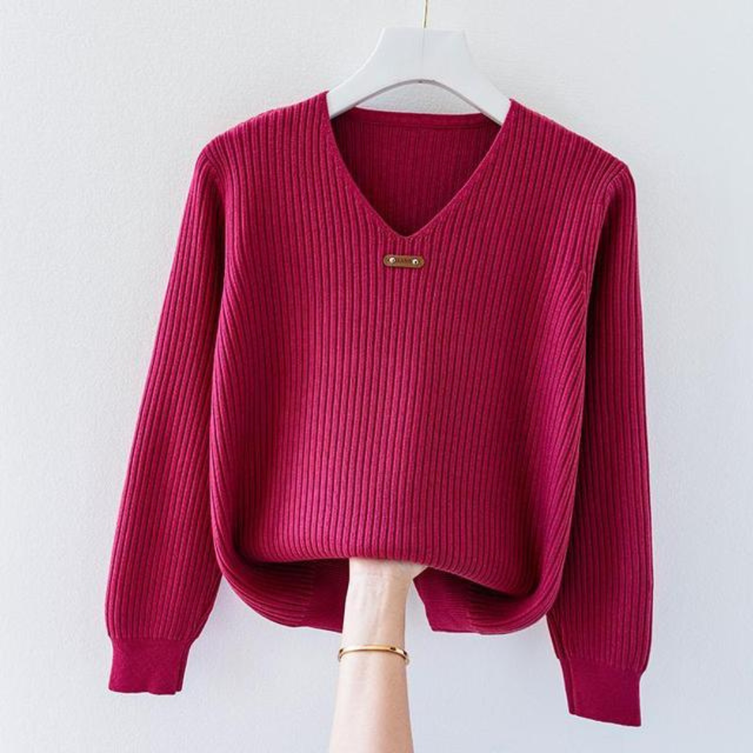 Pull-over rouge en tricot côtelé avec col en V, suspendu sur un cintre blanc. Mode automne-hiver, vêtement chaud et élégant pour femmes.