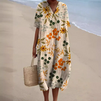 Robe d'été fleurie avec motifs orange et verts, portée sur une plage. Sac en osier à la main. Mode plage, tenue décontractée, style estival.