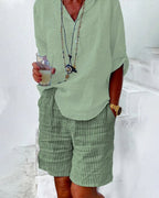 Homme en chemise verte et short rayé, tenant un verre. Style décontracté estival, accessoires tendance, montre dorée. Mode masculine élégante.