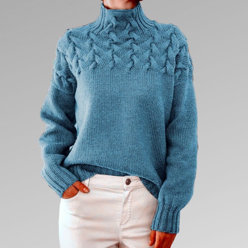 Pull bleu en laine torsadée, col montant, manches longues, porté avec un jean blanc. Mode automne-hiver, style décontracté et élégant.