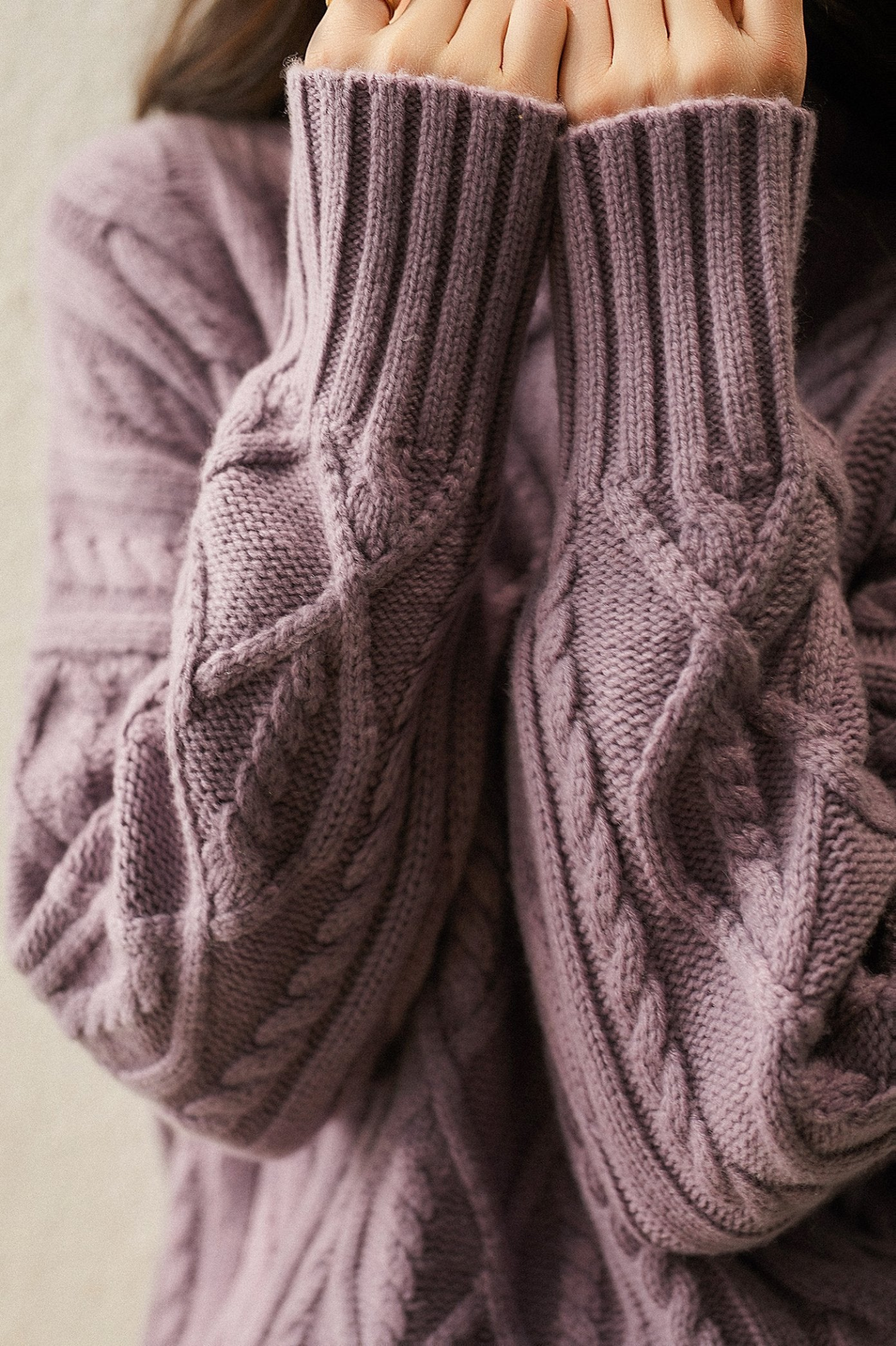 Femme portant un pull en laine tricoté violet avec motifs torsadés, manches longues et col roulé, mode automne-hiver, confort et élégance.