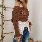Femme portant un pull tricoté marron, style bohème, avec épaules dénudées, sur un haut blanc et un jean. Mode automne, tendance tricot.