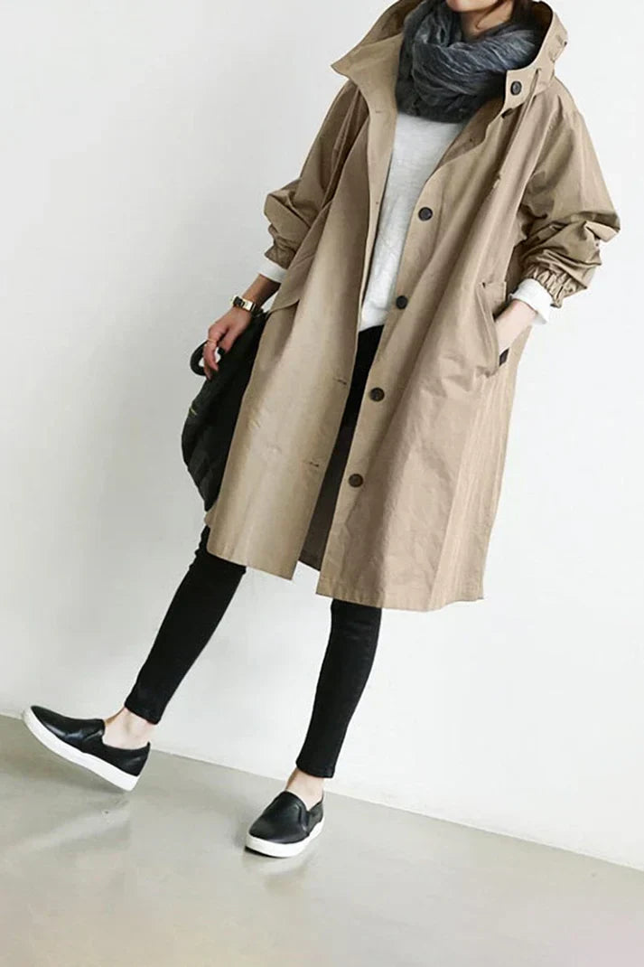 Personne portant un trench-coat beige, écharpe grise, pantalon noir et baskets noires. Mode automne, style décontracté, tendance urbaine.