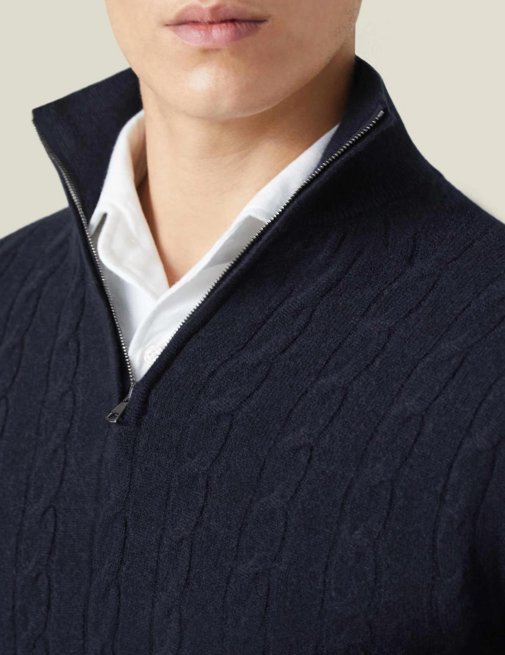 Homme portant un pull bleu marine à col zippé et motif torsadé, sur une chemise blanche. Mode masculine élégante et moderne.
