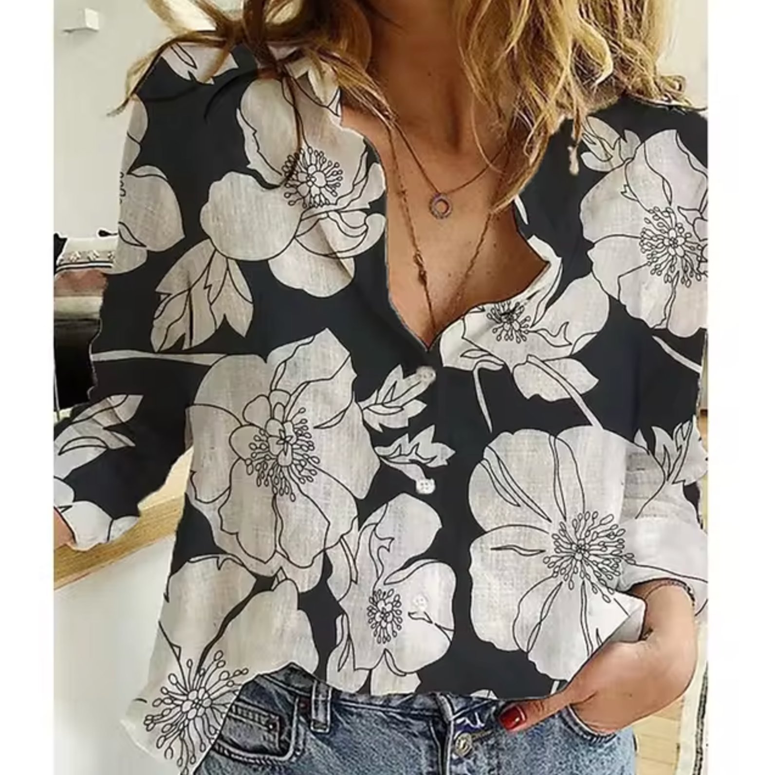 Chemisier à fleurs blanches sur fond noir, manches longues, col en V, porté par une femme avec un collier, style décontracté et tendance.