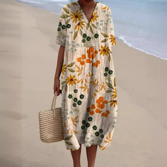 Robe d'été fleurie avec motifs orange et verts, portée sur une plage. Sac en osier à la main. Mode plage, tenue estivale élégante.