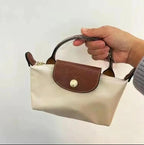 Sac à main beige et marron en cuir, porté par une main. Design élégant, compact, idéal pour la mode féminine. Accessoire tendance et pratique.
