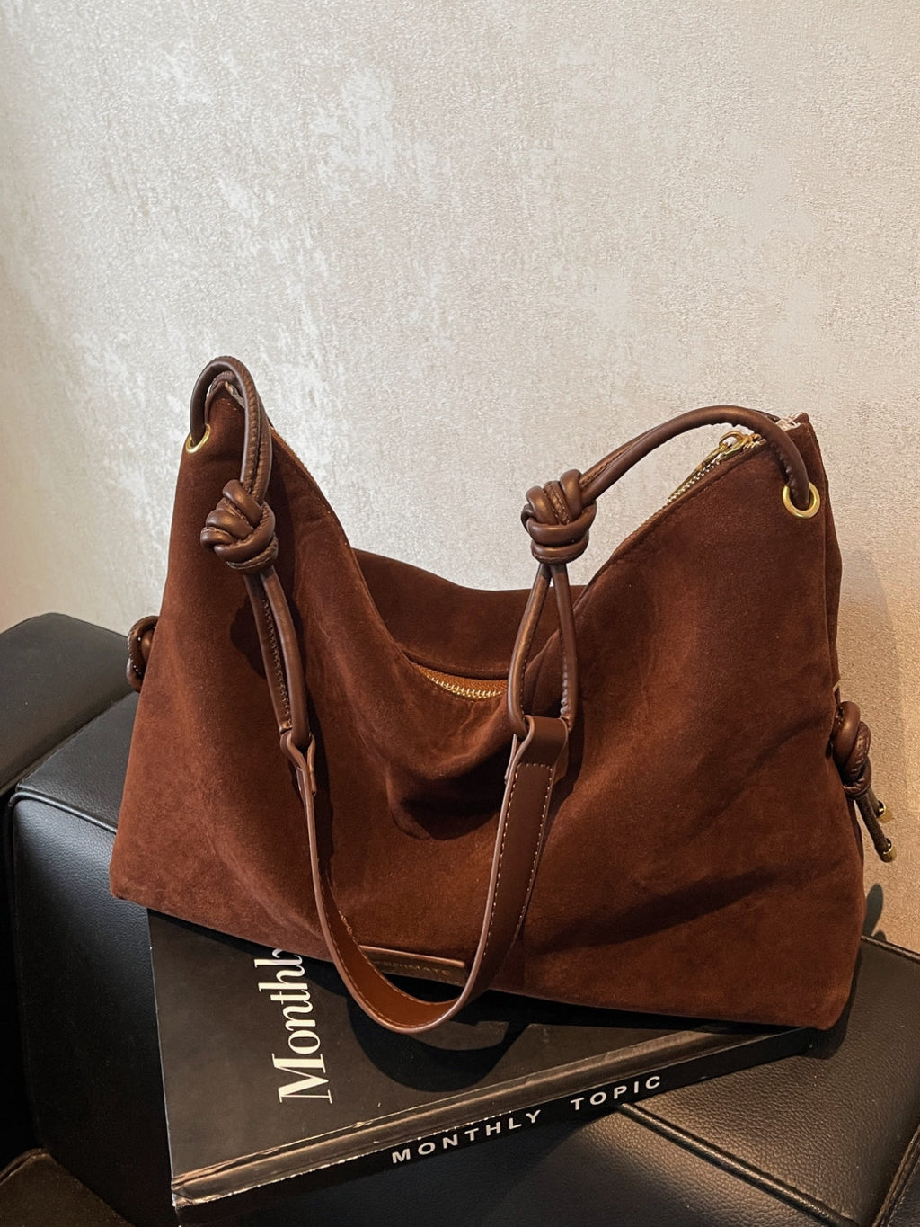 Sac à main en daim marron sur une boîte noire, avec poignées en cuir nouées. Accessoire mode élégant, tendance automne, style chic et sophistiqué.