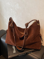 Sac à main en daim marron sur une boîte noire, avec poignées en cuir nouées. Accessoire mode élégant, tendance automne, style chic et sophistiqué.