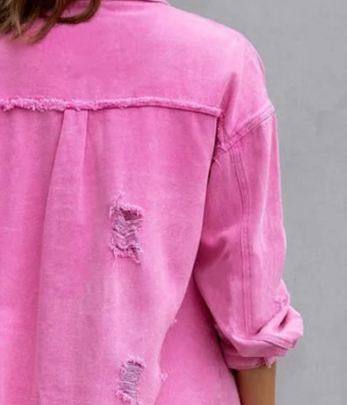 Veste en jean rose usée avec manches retroussées, montrant des déchirures stylisées à l'arrière. Mode décontractée, tendance vintage.