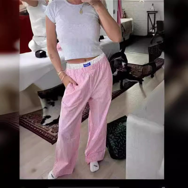 Femme portant un t-shirt blanc et un pantalon rayé rose, posant dans une chambre moderne. Mode décontractée, style quotidien, intérieur élégant.