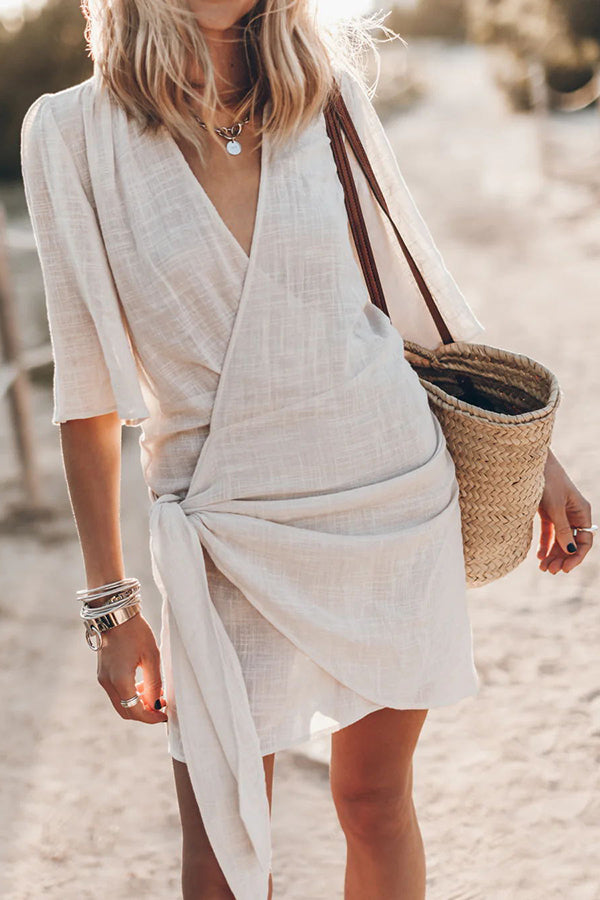 Robe d'été blanche en lin, style portefeuille, manches courtes, portée par une femme avec un sac en osier. Mode estivale chic et décontractée.