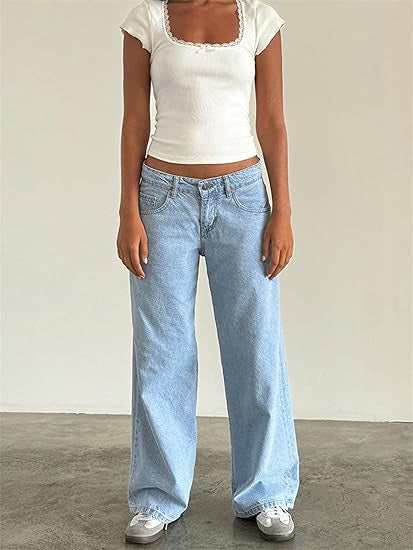 Femme portant un t-shirt blanc ajusté et un jean large bleu clair, debout sur un sol en béton. Mode décontractée, style urbain tendance.