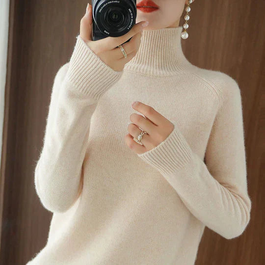 Femme portant un pull col roulé beige, bague et boucles d'oreilles perles visibles. Mode automne-hiver, style élégant et chic.