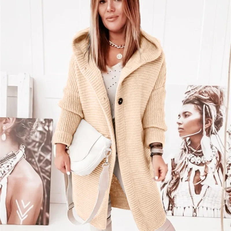 Femme portant un manteau en laine beige avec capuche, sac blanc, posant devant des portraits artistiques. Mode automne-hiver, style chic et décontracté.