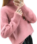 Femme portant un pull en laine rose doux, manches longues, col montant, accessoirisé de bagues argentées et collier, mode automne-hiver tendance.