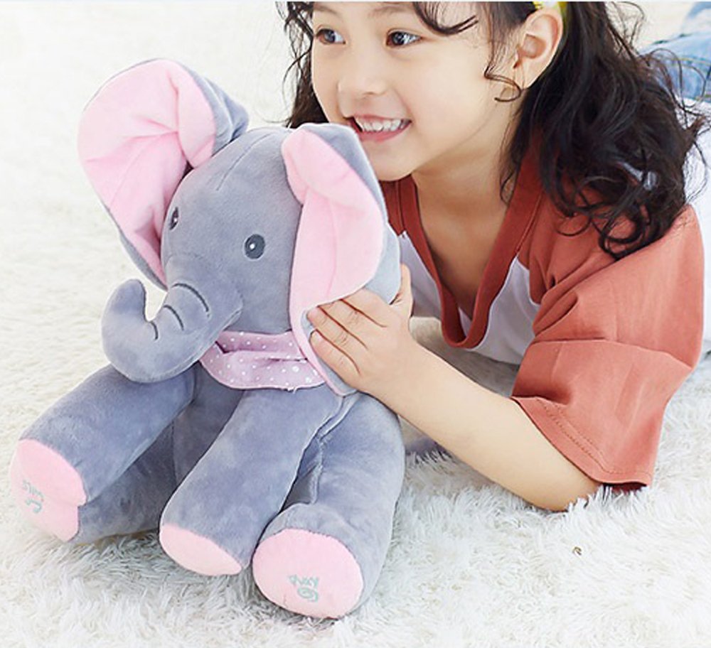 Enfant souriante avec peluche éléphant gris et rose, jouant sur un tapis blanc. Jouet doux, cadeau idéal pour enfants, décoration chambre bébé.