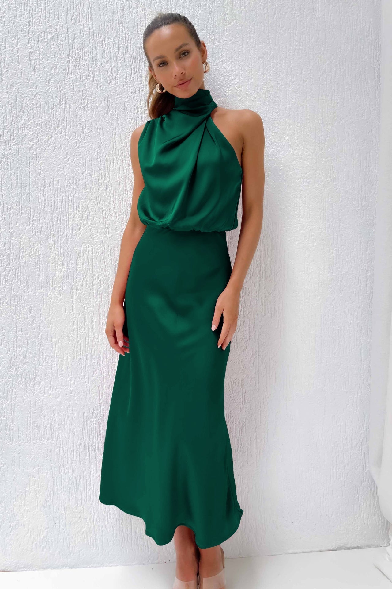 Robe longue verte élégante, sans manches, col haut, portée par une femme sur fond blanc texturé. Mode féminine chic, tenue de soirée.