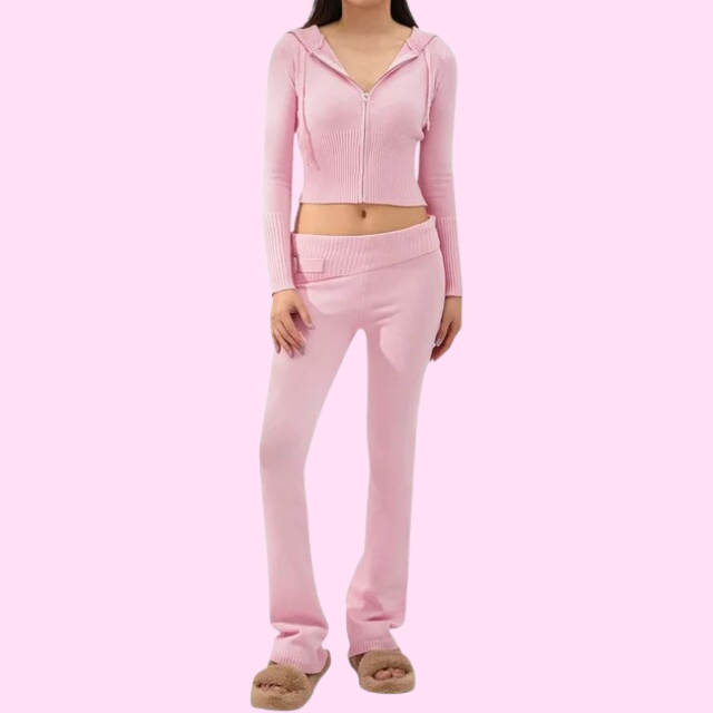 Femme en ensemble de survêtement rose, comprenant un sweat à capuche zippé et un pantalon taille basse, posant sur fond rose. Mode décontractée féminine.
