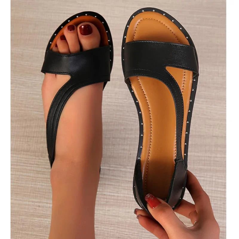 Sandales noires en cuir pour femme avec clous décoratifs, design élégant et moderne, vue de dessus sur fond clair, pédicure rouge visible.