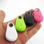 Quatre porte-clés traqueurs Bluetooth colorés (blanc, vert, noir, rose) dans une main, utilisés pour localiser des objets perdus.