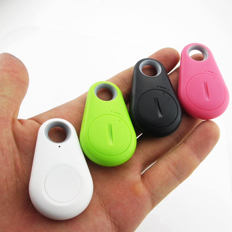 Quatre porte-clés traqueurs Bluetooth colorés (blanc, vert, noir, rose) dans une main, utilisés pour localiser des objets perdus.