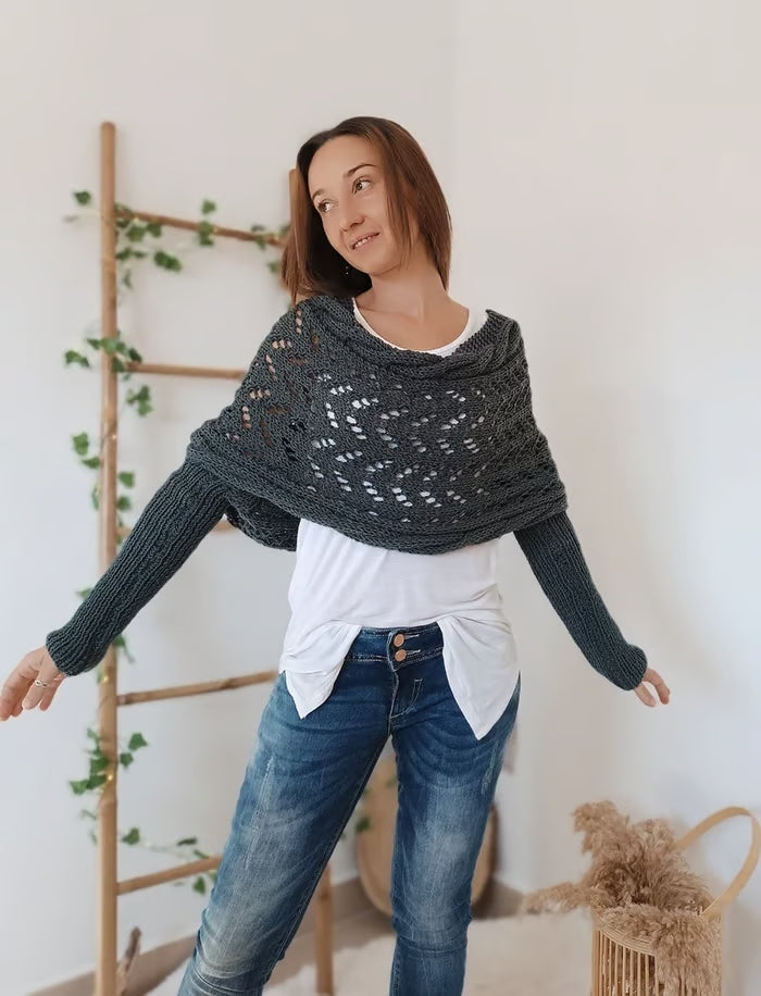 Femme portant un pull en tricot gris, posant devant une échelle en bois décorée de plantes vertes. Mode automne-hiver, style décontracté.